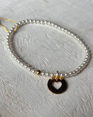 Pearl bracelet with a gold heart pendant on a pink background