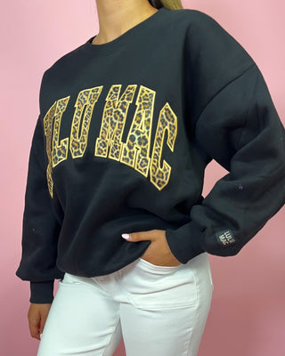 Black sweatshirt with gold leopard print text on a pink background