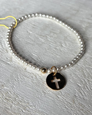 Pearl bracelet with a black and gold charm featuring a cross on a gray surface