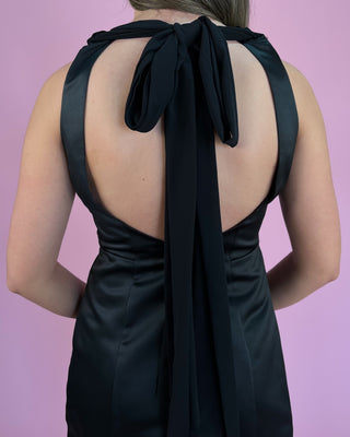 Black dress with open back and ribbon detail on a pink background