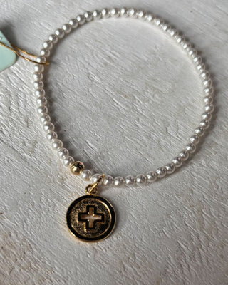 Pearl bracelet with a gold charm on a light gray background