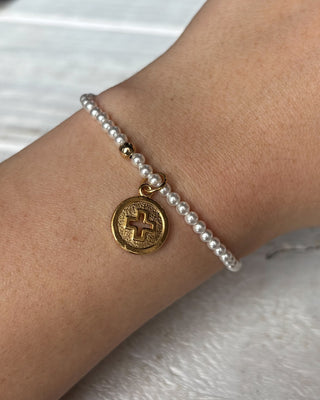 Pearl bracelet with a gold coin charm on a wrist against a white background