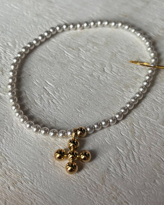 Pearl necklace with a gold charm on a light wooden surface