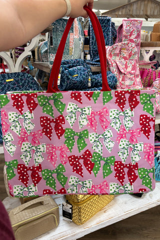 Pink tote bag with green and red bow pattern held by a person in a store setting.