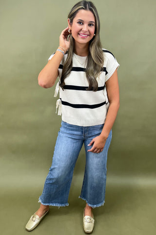 Black and white striped knit top with side bow details styled with light wash wide leg frayed hem jeans and gold loafers.