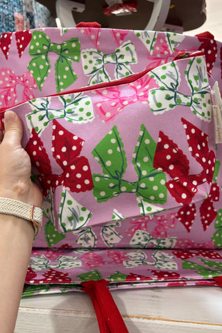 Pink bag with green and red bow patterns held by a hand.