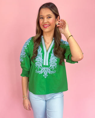 Woman wearing a green blouse with white embroidery against a pink background