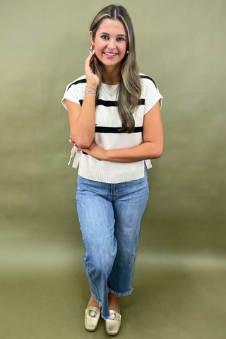 Black and white striped knit top with side bow details styled with light wash wide leg frayed hem jeans and gold loafers.
