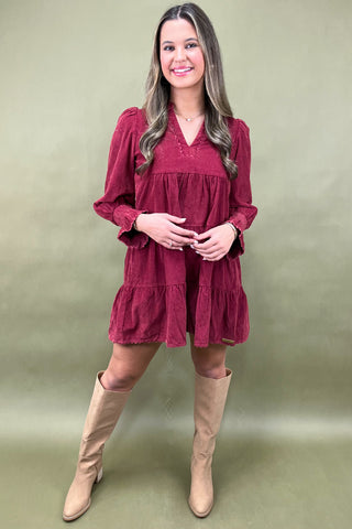 Woman wearing a burgundy dress with ruffled sleeves and beige knee-high boots on a green background