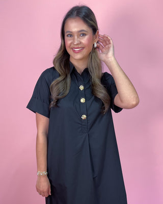 Woman wearing a black dress with gold buttons against a pink background