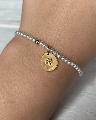 Pearl bracelet with a gold charm on a wrist against a neutral background