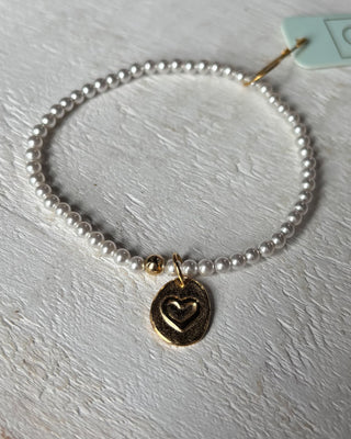 Pearl bracelet with a gold heart charm on a light gray surface