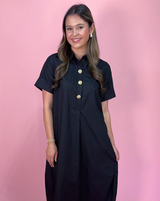 Woman wearing a black dress with gold buttons against a pink background
