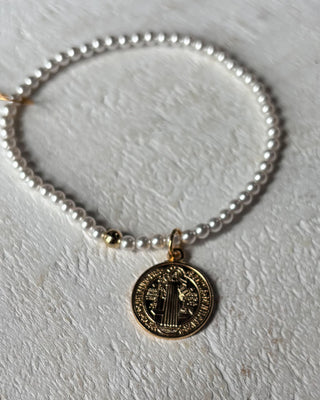 Pearl bracelet with a gold coin charm on a light gray background