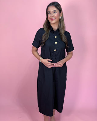 Woman wearing a black dress with gold buttons against a pink background