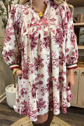 Person wearing a white dress with red floral patterns indoors.