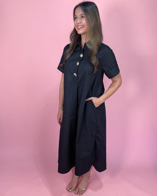 Woman wearing a black dress with gold buttons against a pink background