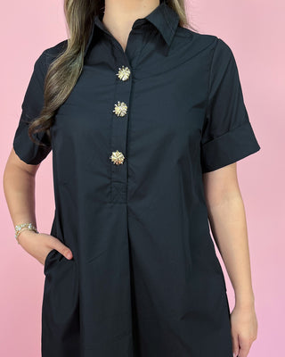 Black dress with gold buttons on a pink background