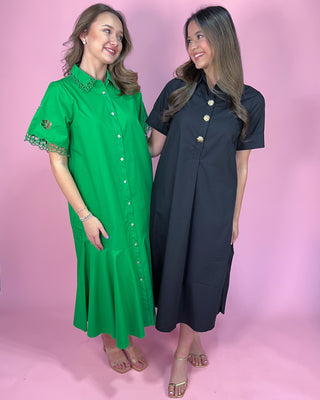 Two women wearing green and navy dresses against a pink background