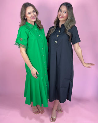 Two women wearing green and black dresses against a pink background