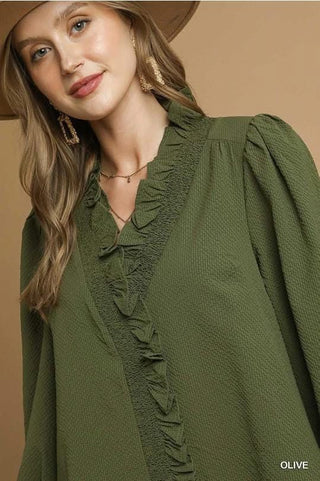 Woman wearing an olive green blouse with ruffled details on a beige background