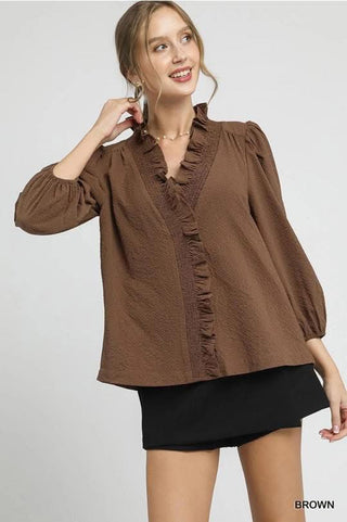 Woman wearing a brown blouse with ruffled details on a white background