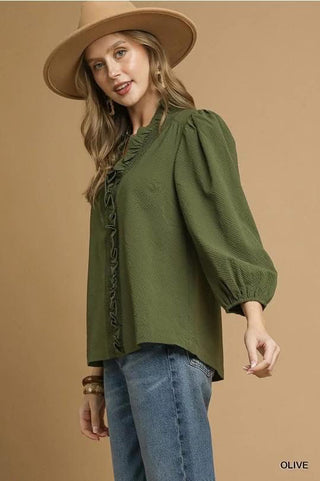 Woman wearing a green blouse with puffed sleeves and a beige hat on a brown background