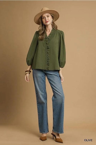 Woman wearing a green blouse, blue jeans, and a beige hat on a brown background