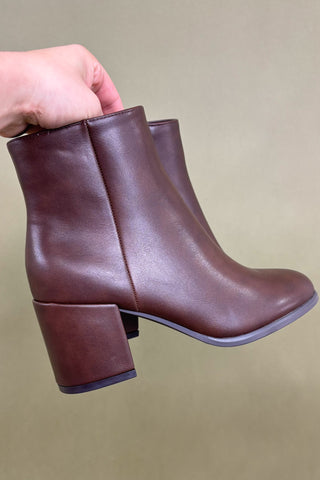 Brown leather ankle boots held by a hand against a beige background