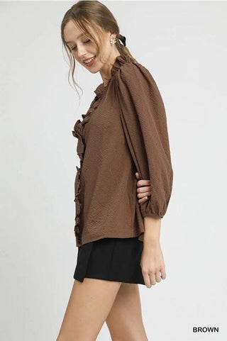 Woman wearing a brown blouse with ruffled details on a white background