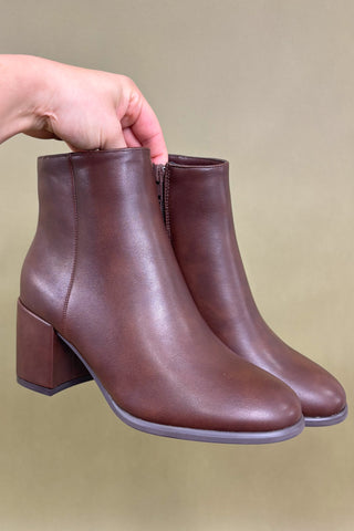 Brown leather ankle boots held by a hand against a beige background