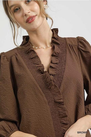 Woman wearing a brown blouse with ruffled details on a white background