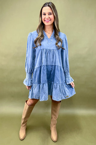 Woman wearing a blue tiered dress with beige boots on a green background
