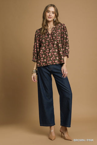 Woman wearing a floral blouse and dark pants against a beige background