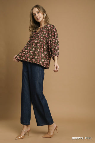 Woman wearing a floral blouse and dark jeans on a brown background