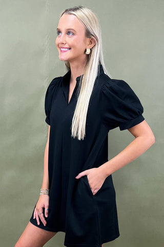 Woman wearing a black dress with puffed sleeves against a green background