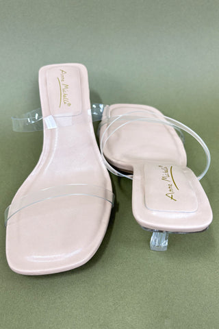 Beige high-heeled shoes with clear straps on a green background