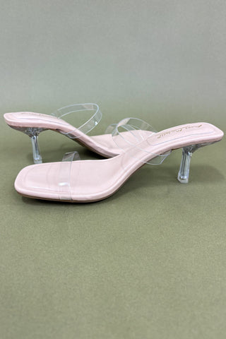 Pair of beige high-heeled sandals with clear heel on a green background