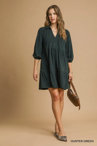 Woman wearing a hunter green dress holding a brown bag on a beige background