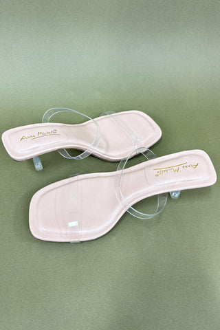 Pair of white sandals with clear straps on a green background