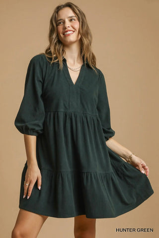Woman wearing a hunter green dress against a beige background