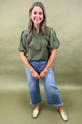 Olive green puff sleeve blouse with split neckline styled with light wash wide leg frayed hem jeans and gold loafers.
