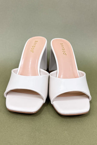 White high-heeled sandals on a green background