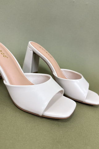 White open-toe high-heeled shoes on a green background