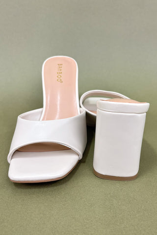 White high-heeled sandals on a green background