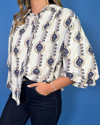 Ivory button-down top with navy and tan botanical print, collared neckline, and ruffle sleeves.