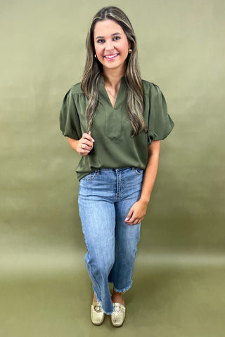 Olive green puff sleeve blouse with split neckline styled with light wash wide leg frayed hem jeans and gold loafers.