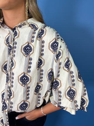 Ivory button-down top with navy and tan botanical print, collared neckline, and ruffle sleeves.