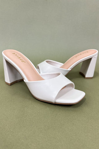 White open-toe high-heeled shoes on a green background