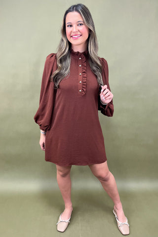 Woman wearing a brown dress with long sleeves against a green background